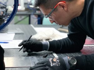 Alumno del curso Montador de Estructuras Aeronáuticas marcando una placa de metal para determinar la distancia a la que debe taladrar